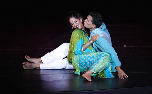 Two Blue13 dancers, one of which is Artistic Director Achinta S. McDaniel, pose for a photo in traditional Indian dress. They are sitting on the ground, centimeters away from a kiss on the cheek.